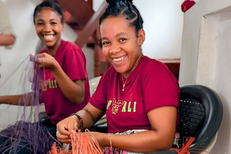 Two smiling CPALI artisans in red shirts sorting dyed raffia fibre for weaving.